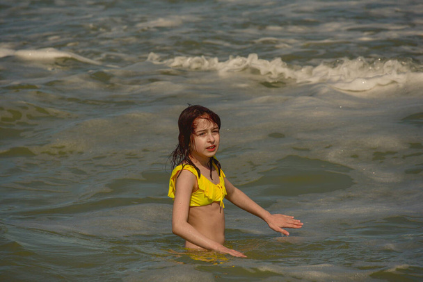 Girl at sea. The portrait of the young girl. Teenager summer vacation sand. Sunny day and the sea. Childhood travel vacation. Teenager in a yellow swimsuit on the beach. Teenager swims in the sea - Photo, Image