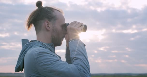 Boční portrét průzkumníka hledícího do dalekohledu na pozadí slunečné oblohy. Muž pozorující divoká zvířata stojící venku na venkově na letních prázdninových cestách. Dobrodružné trekking camping - Záběry, video