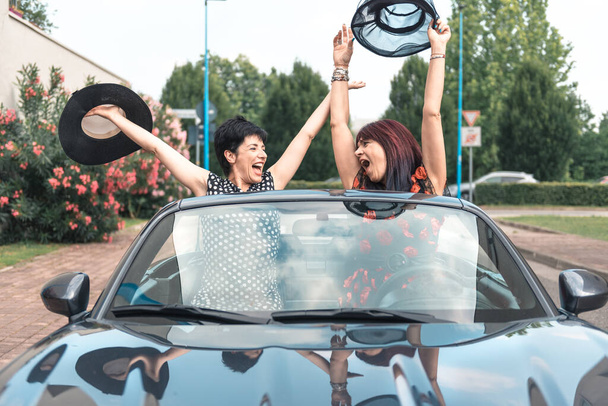 Két elegáns nő vezet egy kabrió autó élvezi a nyaralás szórakozás az úton. - Fotó, kép