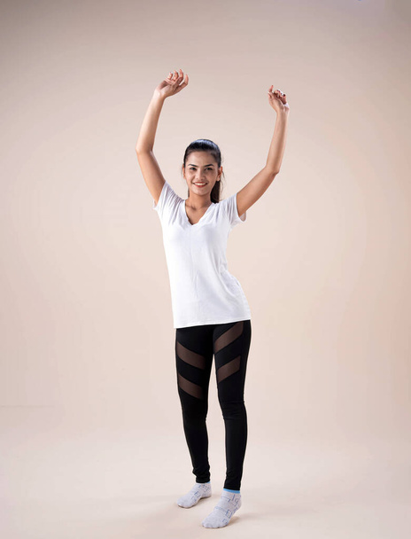 Młoda dama stojąca na rozstaju stóp, lekko skręcona, palcem w dół, podnosząca ręce do góry, tańcząca podstawowy trening, ze szczęśliwym uczuciem - Zdjęcie, obraz