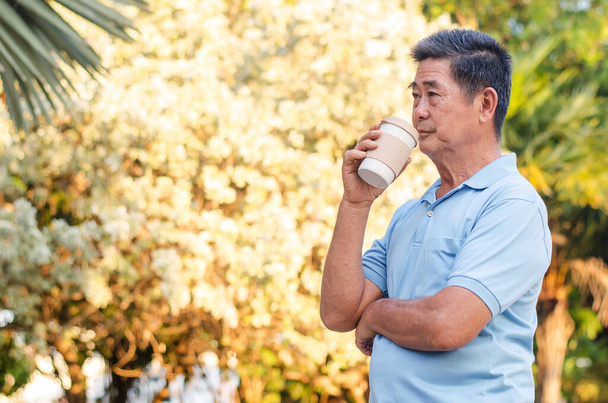 Asiatico signore anziano in piedi nel parco e bere caffè con relax in una giornata di sole - Foto, immagini