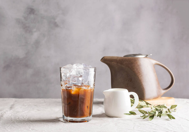 Kalter schwarzer Kaffee mit Eiswürfeln und Milch in einem hohen Glas. Erfrischendes Kaffeegetränk auf dem Tisch grauen Hintergrund. Selektiver Fokuskopierraum aus nächster Nähe. - Foto, Bild