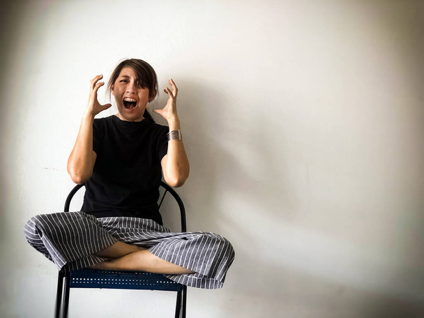 Stressed woman sitting on chair ,raise hands up beside her face,open mouth and scream like crazy,with upset and unhappy feeling,depressive disorder syndrome,serious emotion - Foto, afbeelding