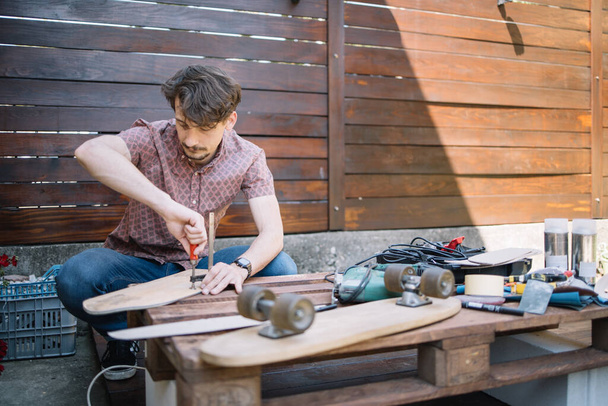Young man working outdoor on table with tools and skateboard - Photo, Image