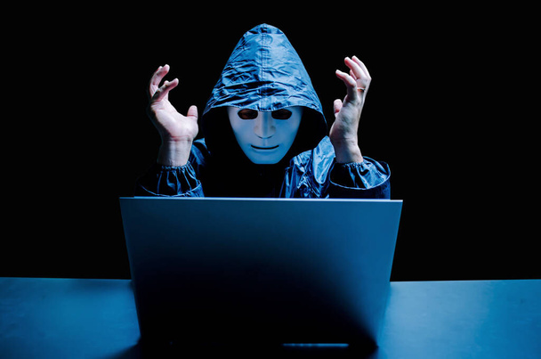 Анонимный компьютерный хакер в белой маске и толстовке. Стрессовый мужчина-хакер кричит на поврежденном ноутбуке, вызванном вирусом, воровством данных, интернет-атакой, темной сетью и концепцией кибербезопасности
. - Фото, изображение