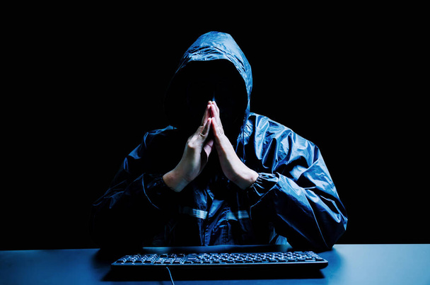 Anonimowy haker komputerowy w białej masce i bluzie. Zasłonięta ciemna twarz z komputerem klawiaturowym w ciemności. Złodziej danych, atak internetowy, koncepcja darknet i cyberbezpieczeństwa. - Zdjęcie, obraz