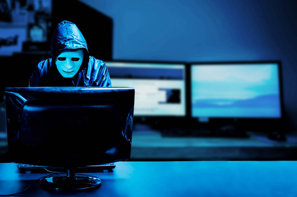 Beyaz maskeli ve kapüşonlu isimsiz bilgisayar korsanı. Karanlık yüz ortada duruyor ve bilgisayar, veri hırsızı, internet saldırısı, darknet ve siber güvenlik konseptiyle bilgisayarı hackliyor.. - Fotoğraf, Görsel