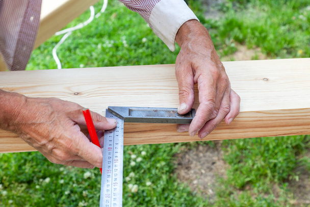 Close-up of male hands holding woodworking marking tool - red pencil and metal ruler on a background of green grass on a summer day. Construction in the country. - Foto, Imagem