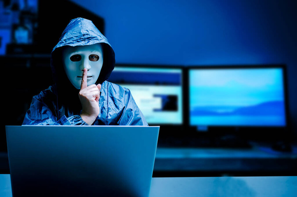 Anonieme computer hacker in wit masker en hoodie. Obscured dark face maakt stilzwijgen gebaar op donkere achtergrond, Data dief, internet aanval, darknet en cyber security concept. - Foto, afbeelding