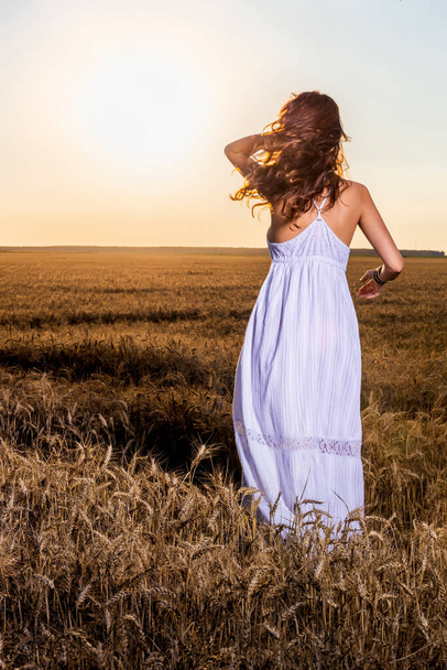 A beautiful woman in a white dress in a wheat field at sunset. - Fotó, kép