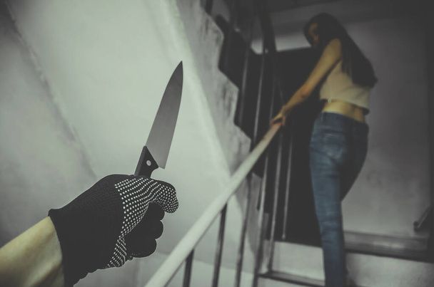 Nieznany przestępca z nożem za młodą dziewczyną na schodach szła do pokoju, Rabunek lub gwałt w koncepcji dzielnicy gangsterskiej, skupienie się na dłoni - Zdjęcie, obraz
