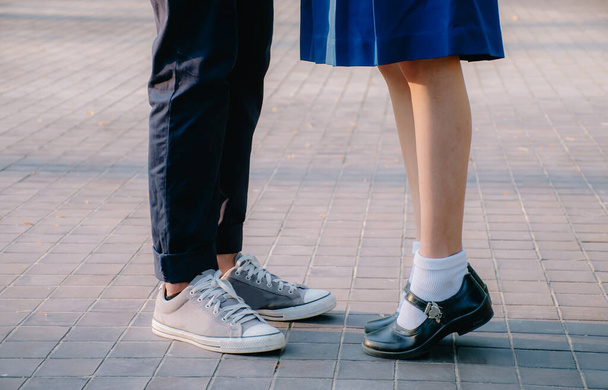Closeup legs and sneakers of young beautiful couple in school uniform standing on the street in park summer evening, Symbol sign couple embracing kissing. Lovers spend time together on romantic date. First teens love and amorousness concept - Photo, Image