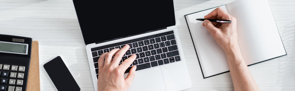 Панорамный снимок человека, печатающего на ноутбуке и пишущего на ноутбуке возле канцелярских принадлежностей и смартфона на столе, зарабатывающего онлайн концепцию - Фото, изображение