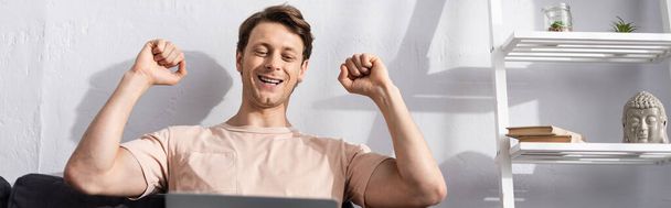 Panoramic crop of happy freelancer showing yes gesture while using laptop at home, earning online concept - Zdjęcie, obraz