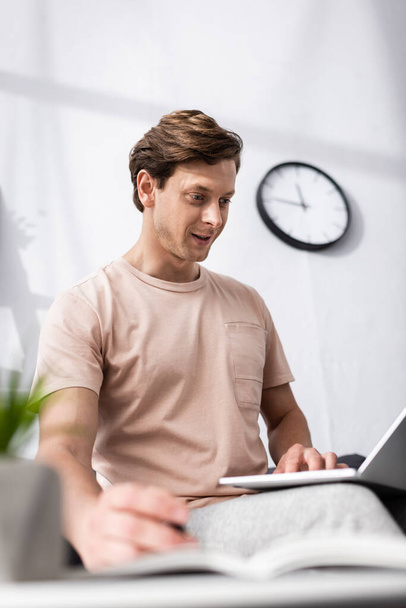 Вибірковий фокус щасливого телефонного працівника, використовуючи ноутбук біля записника на кавовому столі вдома, концепція заробітку в Інтернеті
 - Фото, зображення