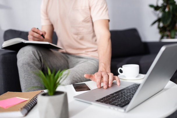 Rajatut näkymä freelancer kannettavan tietokoneen ja kirjallisesti kannettavan lähellä kahvia ja älypuhelinta sohvapöytä, ansaita online-konsepti - Valokuva, kuva