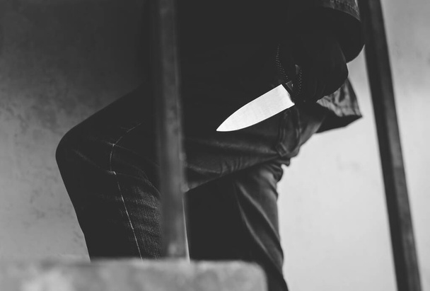 Ασπρόμαυρη φωτογραφία του ληστή να φοράει μάσκα περπατώντας στις σκάλες με μαχαίρι για τα λάφυρα - Φωτογραφία, εικόνα