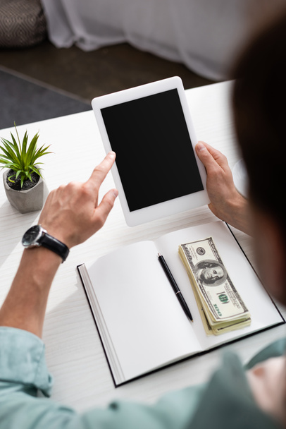 Genç adamın dijital tablet kullandığı seçici odak Masadaki açık defter üzerinde nakit para, online konsept kazanç - Fotoğraf, Görsel