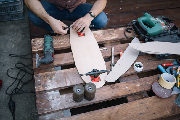 High angle view of man fitting up truck on wooden skateboard - Foto, imagen