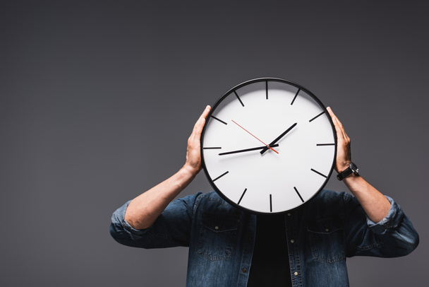 Young man holding wall clock near head on grey background, concept of time management  - Photo, Image