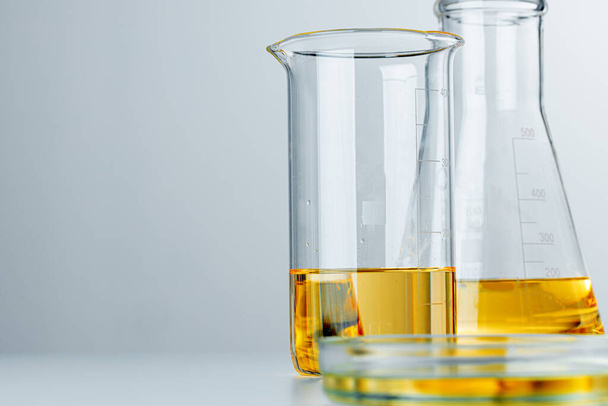 Laboratory glassware with yellow oily liquid on grey background - 写真・画像