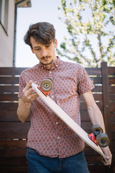 Man checking skateboard wheels while standing in yard - Foto, afbeelding