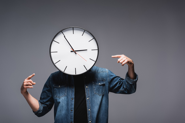 Man with clock near face pointing with fingers on grey background, concept of time management  - 写真・画像