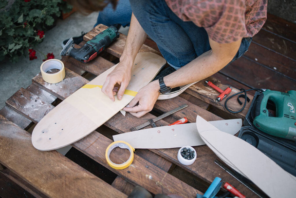 Καλλιεργημένος άνθρωπος κολλήσει ταινία χαρτί στο skateboard στην αυλή - Φωτογραφία, εικόνα