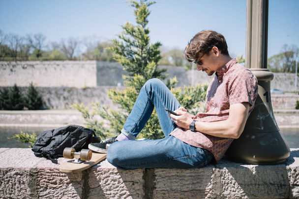 Side view of man sitting on stone sit and looking phone - Foto, afbeelding