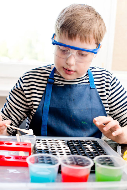 Genç kimyager. Çocuk laboratuarda oynuyor, renkli su ve sodayla deneyler yapıyor. Ödev görevi. - Fotoğraf, Görsel