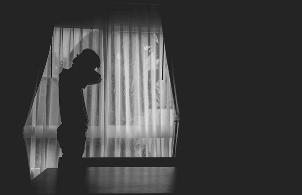 U okna stála osamělá silueta muže se zataženými závěsy v temné komoře. Muž stojí v okně sám, deprese a úzkostná porucha koncept. - Fotografie, Obrázek