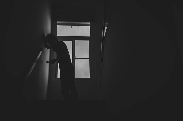 Samotná silueta muže, stojící s telefonem u okna, zavřená v temném domě. Muž stojí v okně sám, deprese a úzkostná porucha koncept. - Fotografie, Obrázek