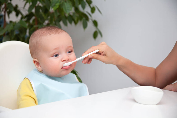 First feeding of baby boy, eat yoghurt, dirty mouth, holds spoon - Photo, Image