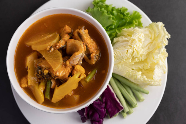 Yellow curry with snakehead fish, Thai food in a bowl on a plate with yard long bean, fried white cabbage, salad and purple cabbage - Фото, изображение