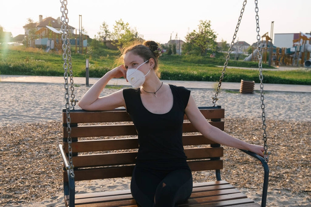 портрет красивой женщины в защитной маске, сидящей на качелях в парке, новая нормальная концепция
 - Фото, изображение