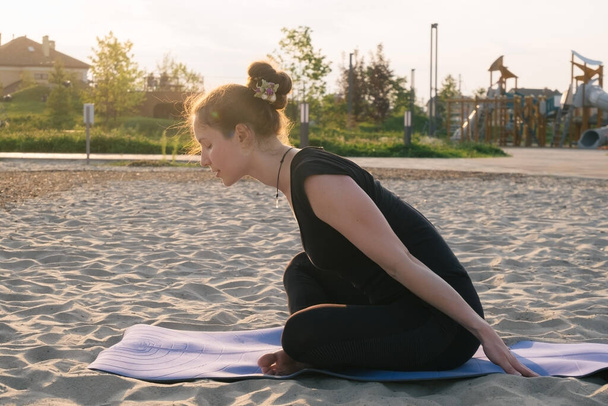 beautiful caucasian woman practising yoga on sand in a city park - Фото, изображение