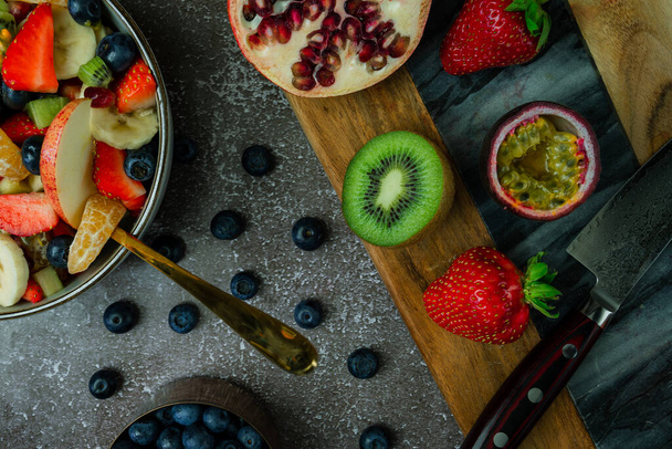 overhead view of fruit salad preparation with wooden chopping board, gold fork and kitchen knife. - Photo, Image