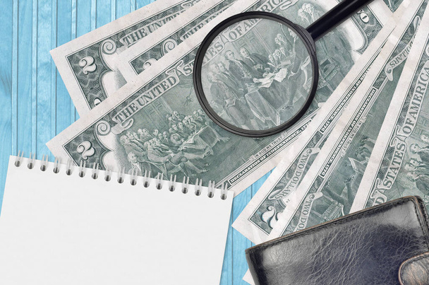 2 US dollars bills and magnifying glass with black purse and notepad. Concept of counterfeit money. Search for differences in details on money bills to detect fake money - Photo, Image