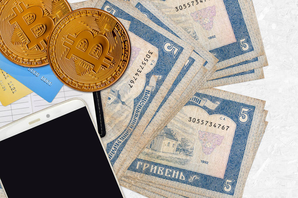 5 factures de hryvnias ukrainiennes et bitcoins dorés avec smartphone et cartes de crédit. Concept d'investissement crypto-monnaie. Opérations minières ou commerciales cryptographiques - Photo, image