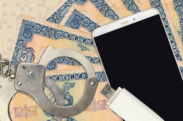 5 ukraińskich hrywien rachunki i smartfon z policyjnymi kajdankami. Koncepcja ataków phishingowych hakerów, nielegalnego oszustwa lub online spyware soft distribution - Zdjęcie, obraz