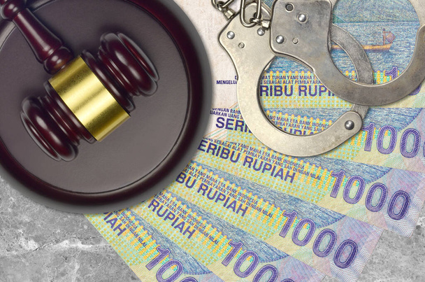1000 Indonesian rupiah bills and judge hammer with police handcuffs on court desk. Concept of judicial trial or bribery. Tax avoidance or tax evasion - Photo, Image