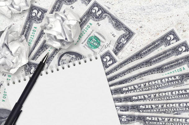 2 δολάρια ΗΠΑ χαρτονομίσματα και μπάλες από τσαλακωμένο χαρτί με σημειωματάριο. Κακές ιδέες ή λιγότερο της έννοιας της έμπνευσης. Αναζήτηση ιδεών για επενδύσεις - Φωτογραφία, εικόνα