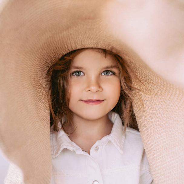 Adorable cheerful little girl in straw hat at home indoor. Fashion, style, childhood, emotions, growing up concept - Foto, afbeelding
