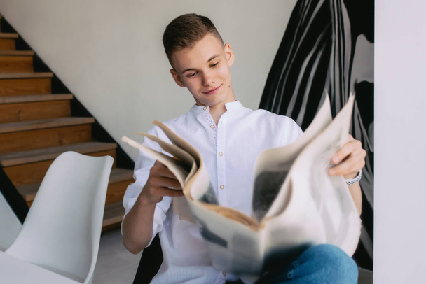 Homem adolescente moderno lendo jornal de papel enquanto café da manhã em casa. Leitura, moda antiga, moderno, conceito de notícias
 - Foto, Imagem