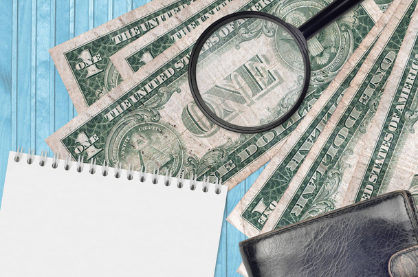 1 US dollar bills and magnifying glass with black purse and notepad. Concept of counterfeit money. Search for differences in details on money bills to detect fake money - Photo, Image