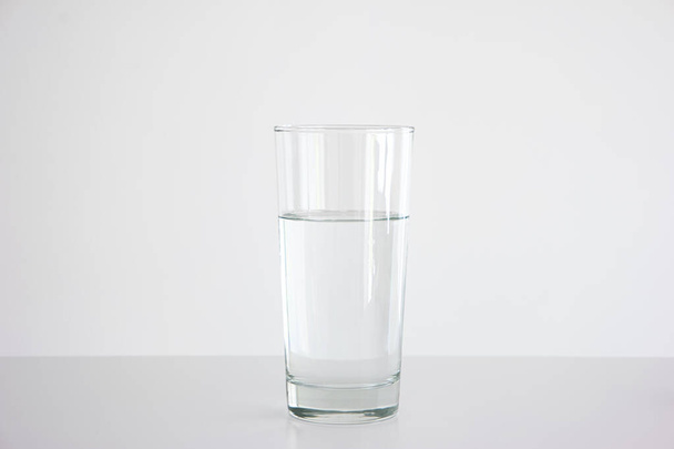 Clear glass three quarters full of water set on white table isolated close up frontal shot 2020 - Zdjęcie, obraz