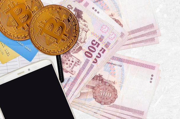 500 Hongaarse forint biljetten en gouden Bitcoins met smartphone en credit cards. Cryptogeld investeringsconcept. Crypto mijnbouw of handel transacties - Foto, afbeelding