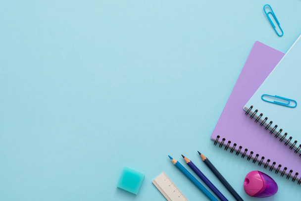 Education flat lay. Top view of blue and purple notebooks, pencil sharpener, clips, eraser, ruler and color pencils. Copy space.  - Фото, изображение