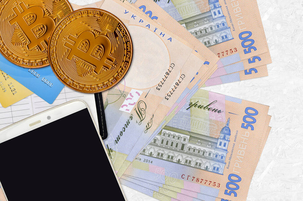 500 Oekraïense hryvnias rekeningen en gouden Bitcoins met smartphone en creditcards. Cryptogeld investeringsconcept. Crypto mijnbouw of handel transacties - Foto, afbeelding