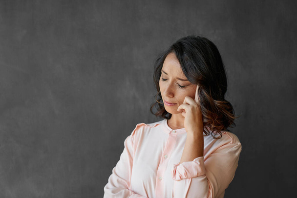 Young businesswoman looking stressed while standing with her eyes closed and a finger on her temple against a chalkboard background - Foto, Bild